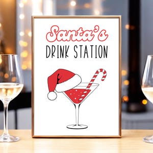 May include: A white sign with a gold frame that says "Santa's Drink Station" in red and black lettering. There is a red and white Santa hat with a martini glass with a red drink and a candy cane.