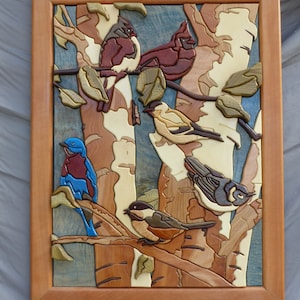 May include: A wooden wall art piece depicting a variety of birds perched on branches. The birds are carved in detail and painted in realistic colors, including red, blue, yellow, and brown. The background is a light blue and white birch tree pattern.