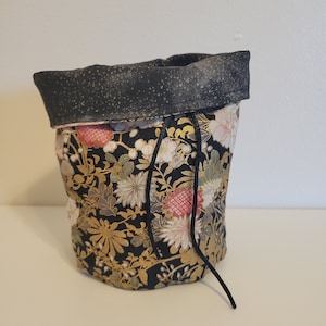 May include: A black drawstring bag with a floral pattern in gold, white, and red. The bag has a black drawstring and a black fabric lining.