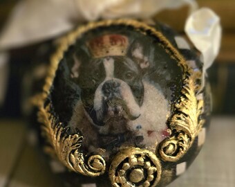 May include: A decorative Christmas ornament featuring a Boston Terrier wearing a crown. The ornament has a black and white checkered pattern with gold accents. A cream-colored ribbon is attached to the top.