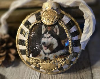 May include: Ornate Christmas ornament featuring a portrait of a Husky dog wearing a crown. The round ornament has a gold and black striped design with gold trim and a white ribbon for hanging. A unique holiday decoration.