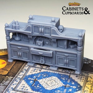 Pode incluir: Uma miniatura cinzenta e detalhada de um arm&aacute;rio de madeira com uma gaveta e portas. O arm&aacute;rio tem uma caveira no topo e est&aacute; etiquetado como "Cabinets & Cupboards" com o logotipo HeroQuest.