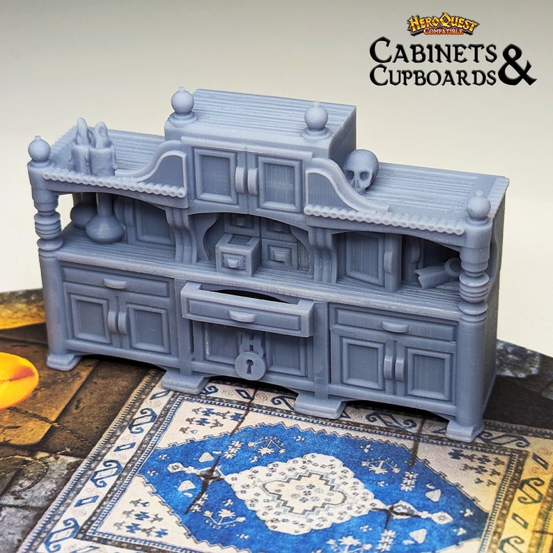 Pode incluir: Uma miniatura cinzenta e detalhada de um arm&aacute;rio de madeira com uma gaveta e portas. O arm&aacute;rio tem uma caveira no topo e est&aacute; etiquetado como "Cabinets & Cupboards" com o logotipo HeroQuest.