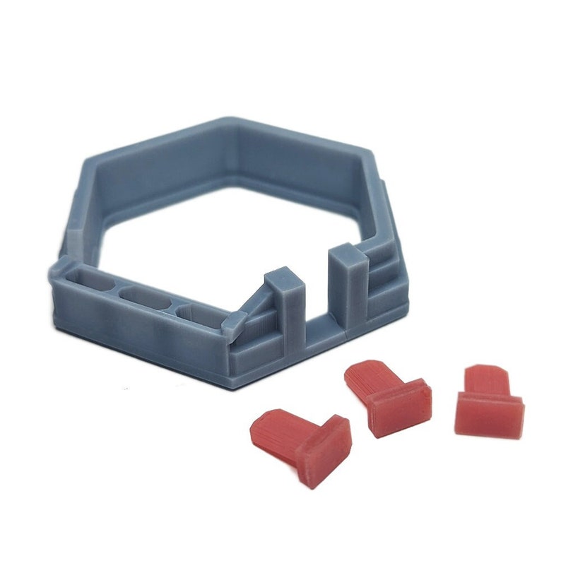 May include: A gray hexagonal plastic base with three red plastic pieces. The base has a small opening on one side. The red pieces are rectangular and have a slightly rounded top.