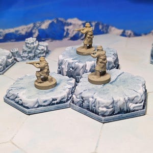 May include: Miniature soldier figurines in tan uniforms, positioned on hexagonal, icy platforms. The figures are holding rifles, with a backdrop of a snowy mountain range. The scene suggests a tabletop war game or diorama, with a focus on detail.