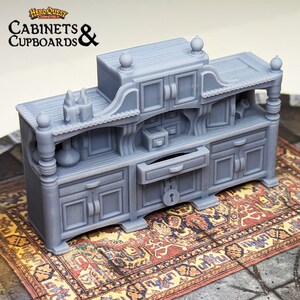 Pode incluir: Um arm&aacute;rio de madeira em miniatura cinza, detalhado, com uma gaveta e v&aacute;rias portas. O arm&aacute;rio tem uma fechadura e &eacute; decorado com entalhes ornamentados. O arm&aacute;rio est&aacute; sentado em um tapete estampado.