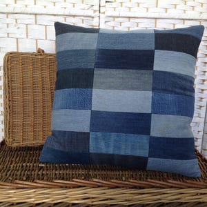 May include: A square throw pillow featuring a patchwork design composed of rectangular denim fabric strips in various shades of blue, ranging from light sky blue to deep navy, arranged in a structured grid pattern across the entire surface.