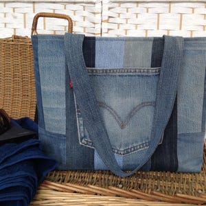 May include: A denim tote bag made from repurposed jeans. The bag features a front pocket, a red Levi's tag, and a woven handle. The bag is approximately 38 cm wide and 30 cm tall.