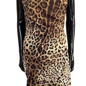 May include: A sleeveless knee-length dress featuring a brown and black leopard print pattern. The garment has a boat neckline with structured pleating across the bodice and waist, creating a fitted silhouette that falls to a straight hemline.