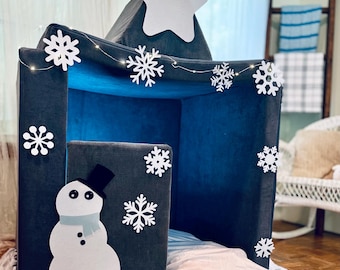 May include: A gray and blue playhouse tent with a white star on top and white snowflake decorations. A snowman cutout is on the front of the tent.