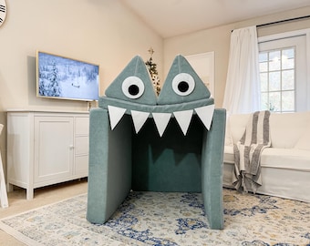 May include: A teal blue monster-shaped playhouse for kids with white teeth and large black eyes. The playhouse is made of soft fabric and is perfect for indoor play.