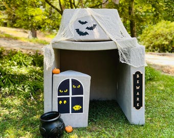 May include: A gray playhouse shaped like a haunted house with a black cauldron, orange pumpkins, and a sign that says "BEWARE".