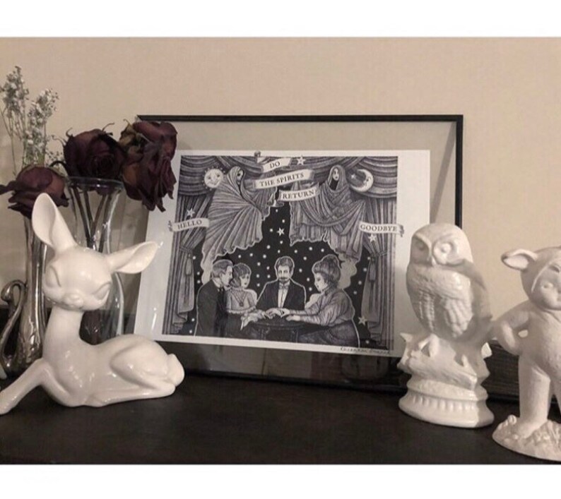 May include: A black and white print in a black frame depicting a group of people sitting around a table with a ghost hovering above them. The print reads "Do the Spirits Return" and is framed with a black frame.
