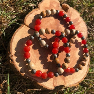 May include: Three beaded bracelets with red, brown, and gray beads. The bracelets are stacked on top of each other on a wooden surface.