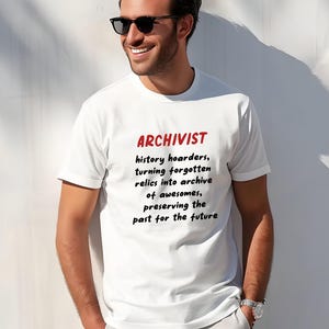 May include: White t-shirt with the word "ARCHIVIST" in red, above a black text description. The text reads "history hoarders, turning forgotten relics into archive of awesomes, preserving the past for the future."