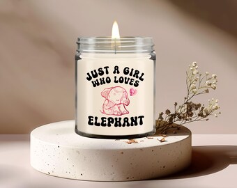 Könnte beinhalten: Eine weiße Kerze in einem Glasgefäß mit einer Illustration eines rosa und weißen Elefanten und dem Text "Just a girl who loves elephant".