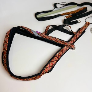 以下が含まれることがあります： 黒と赤の模様のついた犬用ハーネス。金属製のリングと黒いストラップが付いています。ハーネスはトレーニング用で、緑と白のポールが付いた長い黒いストラップが付いています。