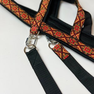 以下が含まれることがあります： 赤と金の模様のついたストラップと2つの金属製クリップが付いた黒い犬用ハーネス。ハーネスはメッシュデザインで、耐久性のある素材で作られています。