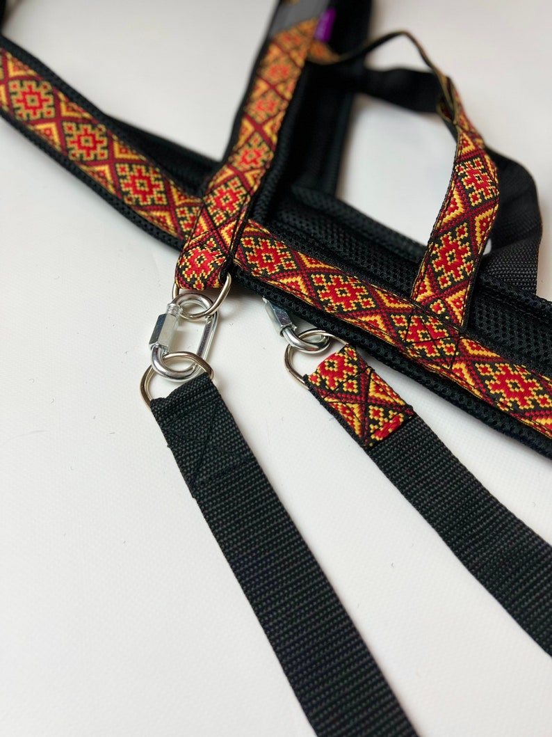 以下が含まれることがあります： 赤と金の模様のついたストラップと2つの金属製クリップが付いた黒い犬用ハーネス。ハーネスはメッシュデザインで、耐久性のある素材で作られています。