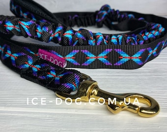 Puede incluir: Correa para perro negra y azul con estampado y un clip de metal dorado. La correa tiene una sección de cordón elástico y el texto "ICE-DOG" es visible en la correa.