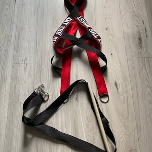 May include: Red and black exercise straps with the text "I AM THE BEAST" printed on them. The straps are attached to a white wooden dowel.