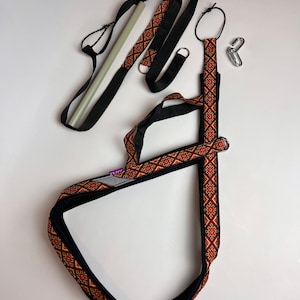 以下が含まれることがあります： 黒と赤の模様のストラップ、黒いストラップ、白いポール。ストラップには金属製のリングとフックが付いています。