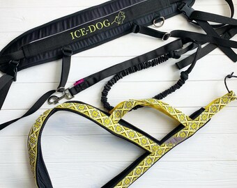 May include: A black and yellow dog harness with a black belt and a black leash. The harness has a geometric pattern and the belt has the text "ICE-DOG" on it. The leash has a springy section and a metal clip.