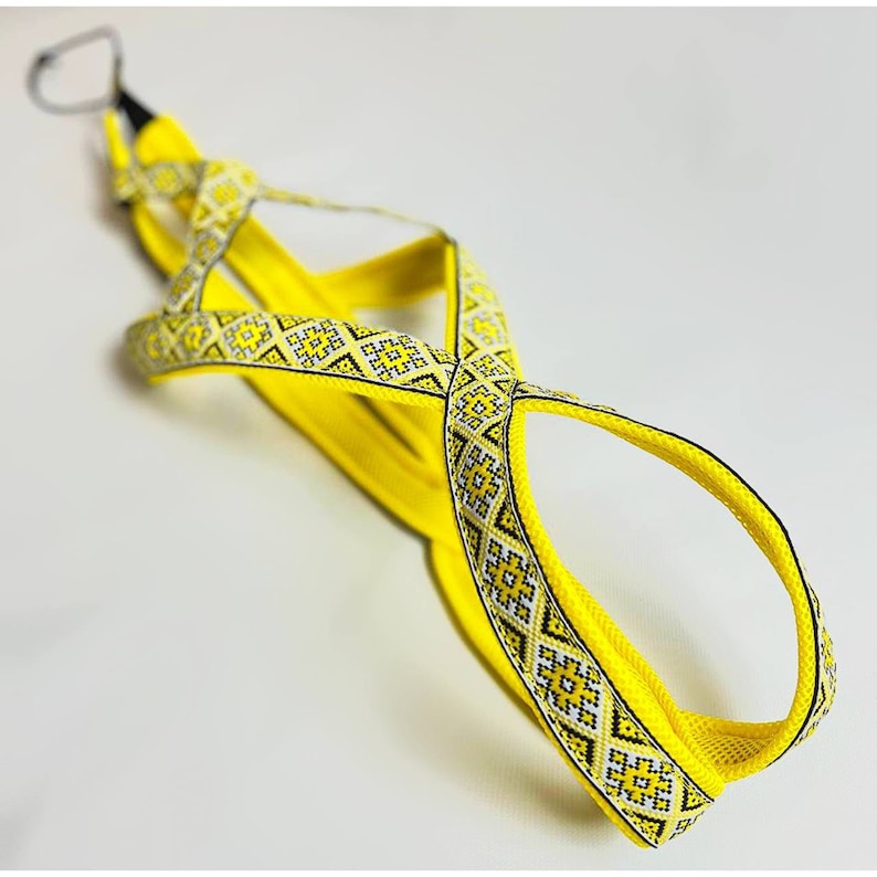 May include: Yellow camera strap with a geometric pattern. The strap is made of woven fabric and has a black and white design.