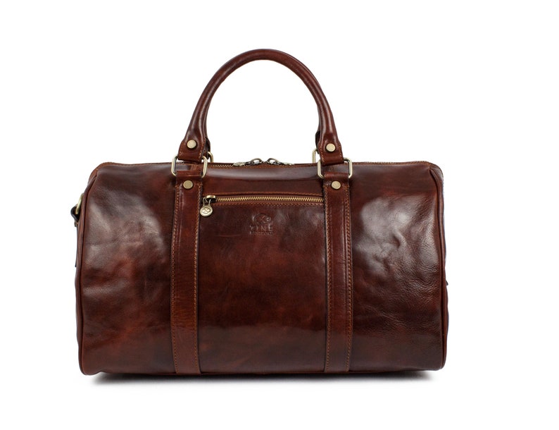 May include: A brown leather duffel bag with gold hardware and a zipper closure. The bag has a top handle and a shoulder strap.