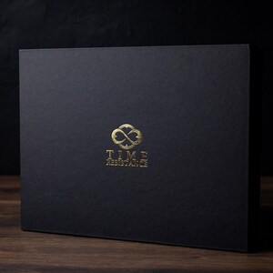 Puede incluir: Una caja rectangular negra con un logotipo dorado que dice "TIME RESISTANCE". El logotipo presenta un dise&ntilde;o de s&iacute;mbolo de infinito. La caja est&aacute; sobre una superficie de madera.