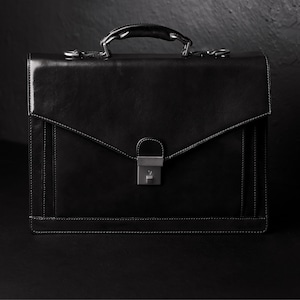 May include: A black leather briefcase with a silver clasp and a handle. The briefcase has a flap that closes with a buckle.