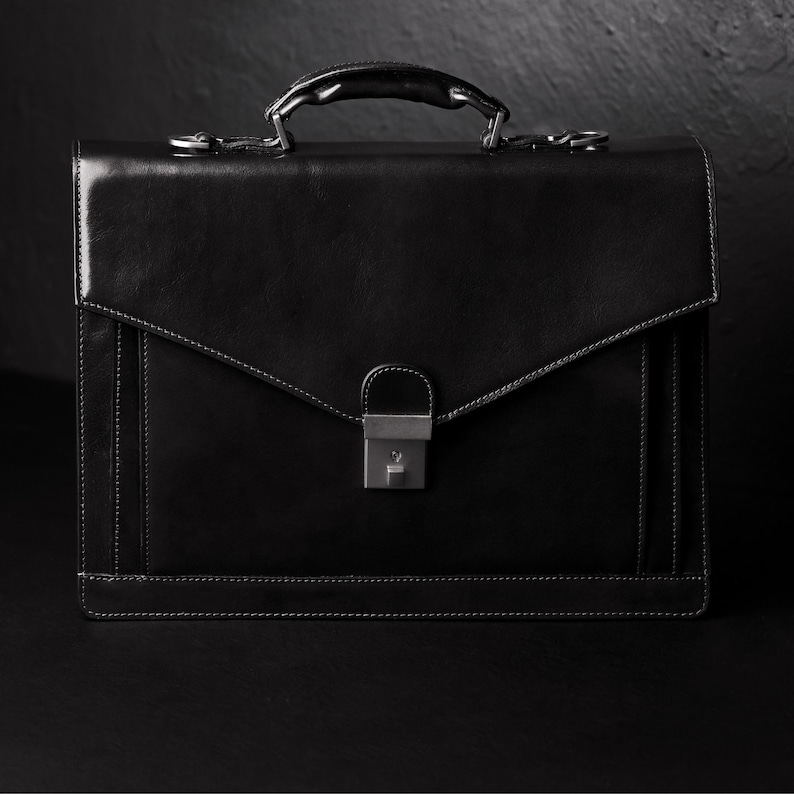 May include: A black leather briefcase with a silver clasp and a handle. The briefcase has a flap that closes with a buckle.