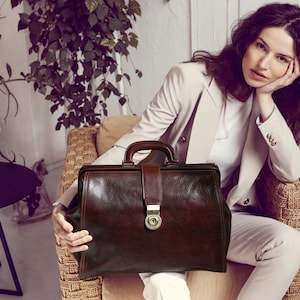 May include: A brown leather doctor's bag with a brass lock and handle. The bag is sitting on a wicker chair.