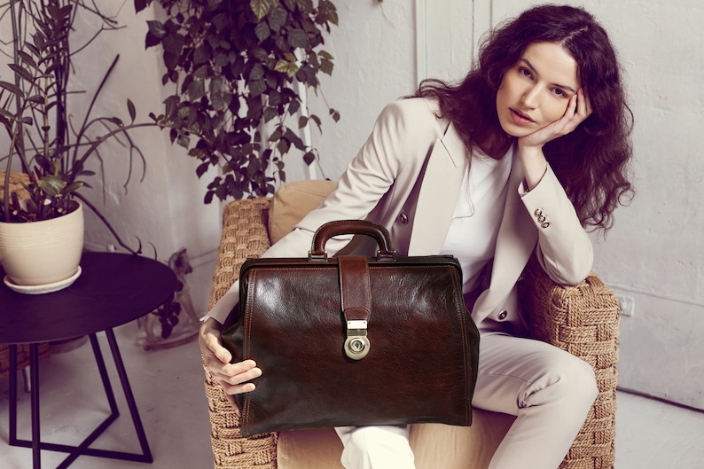 May include: A brown leather doctor's bag with a brass lock and handle. The bag is sitting on a wicker chair.