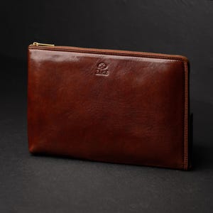 Puede incluir: Un malet&iacute;n de documentos de cuero marr&oacute;n con cierre de cremallera dorada. El estuche tiene un acabado liso y pulido y un peque&ntilde;o logotipo en relieve en la parte superior. El cuero es de un color marr&oacute;n rico y c&aacute;lido, lo que sugiere calidad y artesan&iacute;a.