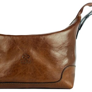 May include: A brown leather travel bag with a zipper closure and a top handle. The bag has the text "TIME TRAVELERS" embossed on the front.