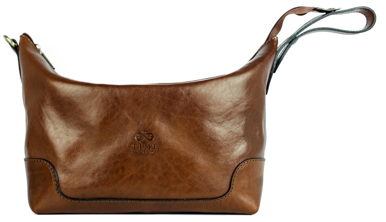 May include: A brown leather travel bag with a zipper closure and a top handle. The bag has the text "TIME TRAVELERS" embossed on the front.