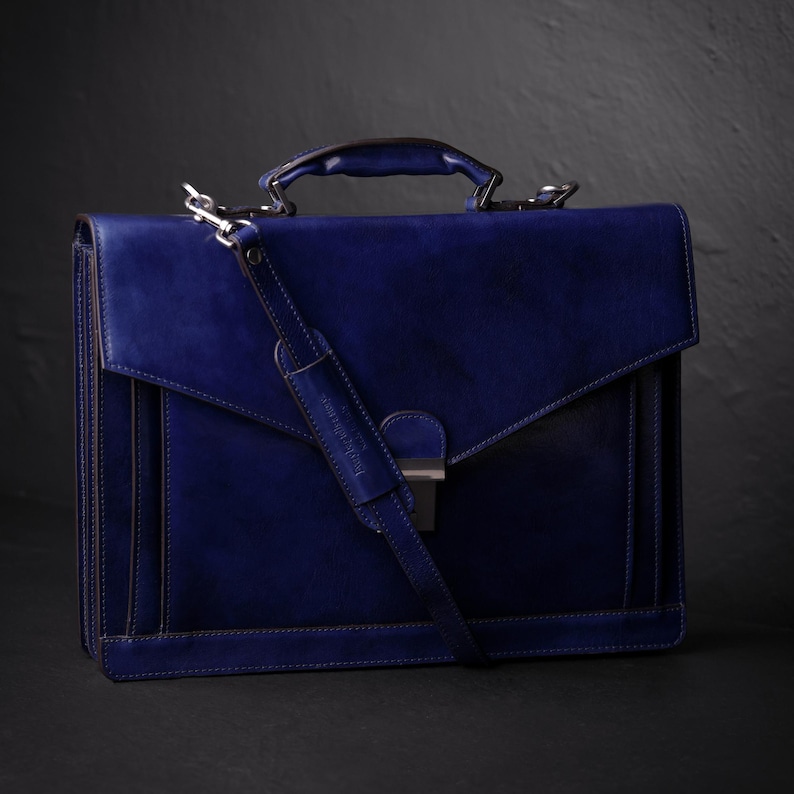 May include: A dark blue leather briefcase with a silver clasp and a long adjustable strap. The briefcase has a flap closure and a top handle.