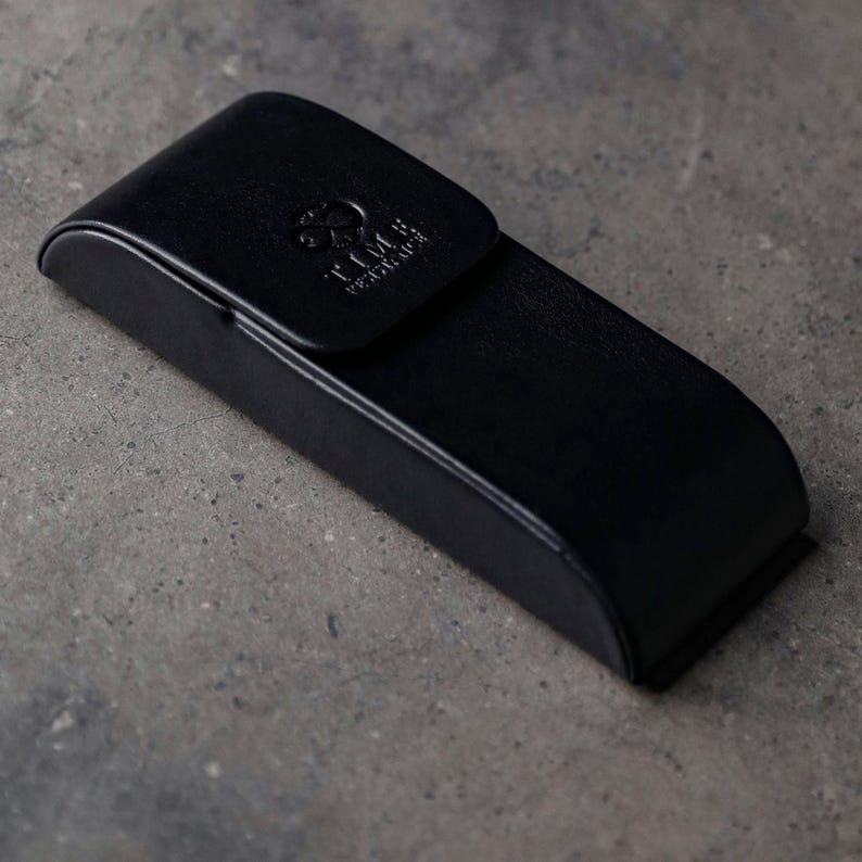 May include: A black rectangular hard-shell case with rounded edges and a hinged lid. The top of the lid features an embossed circular logo and the text TIME WATCHES. The case has a smooth, matte finish and a secure closure mechanism.