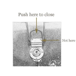May include: Close-up of a leather bag's clasp. The clasp has a metal latch with a small keyhole. The text "Push here to close" is above the clasp, and "Not here" is to the right of the clasp.