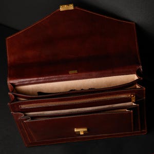 May include: A brown leather briefcase with a gold clasp and zipper. The briefcase is open and has multiple compartments.