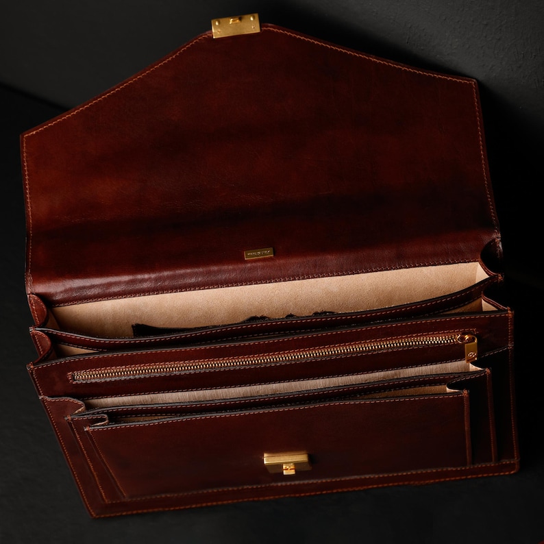 May include: A brown leather briefcase with a gold clasp and zipper. The briefcase is open and has multiple compartments.