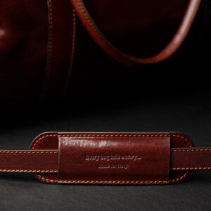 K&ouml;nnte beinhalten: Nahaufnahme eines braunen Lederriemens f&uuml;r eine Tasche mit dem gepr&auml;gten Text "Every bag tells a story... Made in Italy" auf dem Riemen.
