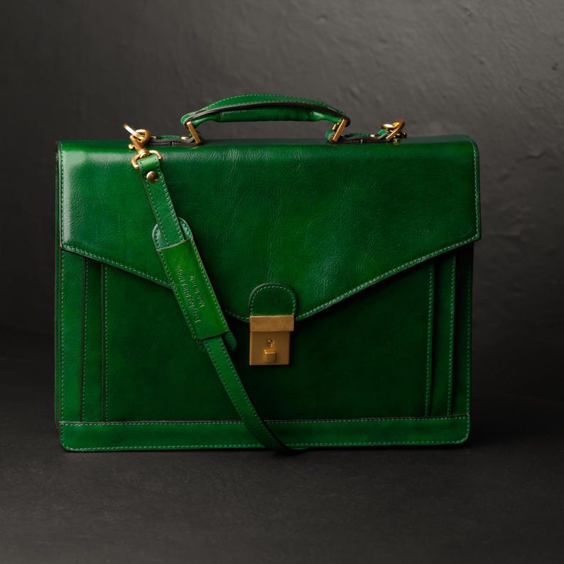 May include: A dark green leather briefcase with a gold clasp and a long adjustable shoulder strap.