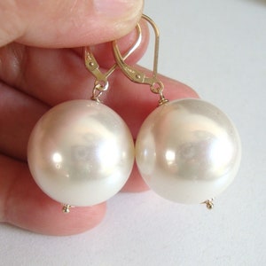 May include: A pair of gold earrings with large, white, round pearl-like drops.