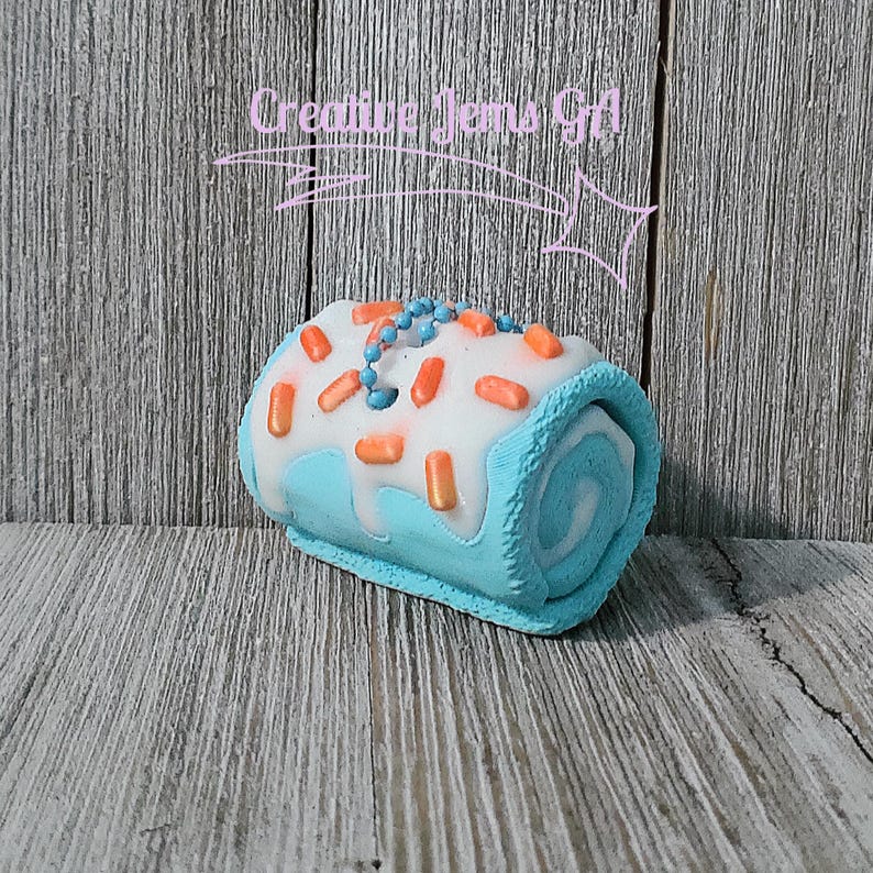 Op de afbeelding: Een blauw-witte decoratieve rolcake met oranje hagelslag en blauwe kraalaccenten. De cake heeft een witte glazuur met oranje hagelslag en blauwe kraalaccenten. De tekst "Creative Gems Gift" staat op de achtergrond.