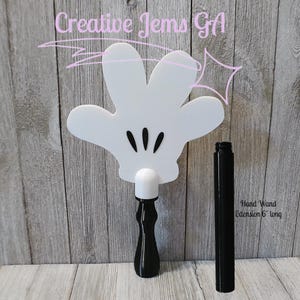 Peut inclure: Une baguette blanche en forme de main avec des d&eacute;tails noirs et une poign&eacute;e noire. La baguette a trois lignes noires repr&eacute;sentant les doigts. Une extension noire s&eacute;par&eacute;e de 15 cm est incluse. Le texte "Creative Jems GA" est visible.