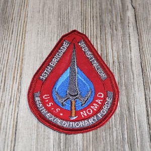 May include: A red, gray, and blue embroidered patch with the text "18th Brigade 3rd Battalion U.S.S. Nomad 45th Expeditionary Force".