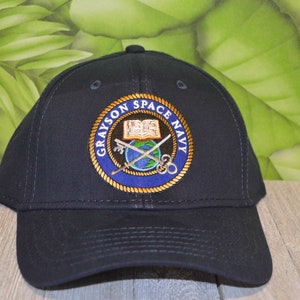May include: A navy blue baseball cap with an embroidered logo that says "Grayson Space Navy" and features a book, crossed keys, a globe, and a compass.
