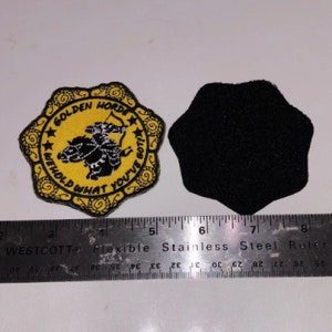 May include: A yellow and black embroidered patch with the text "Golden Horde" and "Behold What You've Got!" around a black silhouette of a person riding a horse. The patch is attached to a black felt backing.